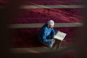 hombre musulmán rezando solo a alá dentro de la mezquita y leyendo el libro sagrado islámico foto