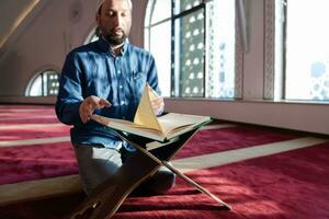 hombre musulmán rezando solo a alá dentro de la mezquita y leyendo el libro sagrado islámico foto