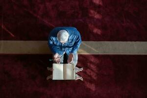 hombre musulmán rezando solo a alá dentro de la mezquita y leyendo el libro sagrado islámico foto