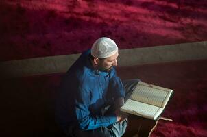 hombre musulmán rezando solo a alá dentro de la mezquita y leyendo el libro sagrado islámico foto