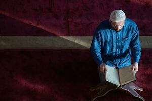 hombre musulmán rezando solo a alá dentro de la mezquita y leyendo el libro sagrado islámico foto