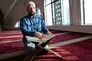 hombre musulmán rezando solo a alá dentro de la mezquita y leyendo el libro sagrado islámico foto