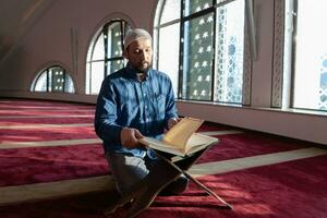 hombre musulmán rezando solo a alá dentro de la mezquita y leyendo el libro sagrado islámico foto