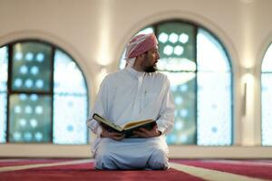 muslim man praying Allah alone inside the mosque and reading islamic holly book photo