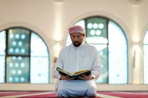 hombre musulmán rezando solo a alá dentro de la mezquita y leyendo el libro sagrado islámico foto