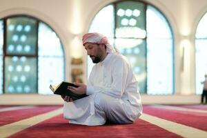 hombre musulmán rezando solo a alá dentro de la mezquita y leyendo el libro sagrado islámico foto