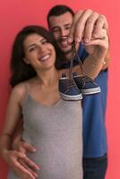 young pregnant couple holding newborn baby shoes photo