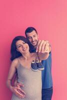 young pregnant couple holding newborn baby shoes photo