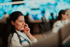 Female security guard operator talking on the phone while working at workstation with multiple displays Security guards working on multiple monitors photo