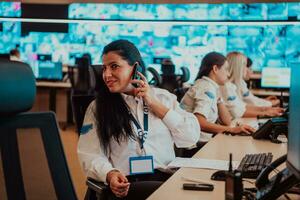 hembra seguridad Guardia operador hablando en el teléfono mientras trabajando a puesto de trabajo con múltiple muestra seguridad guardias trabajando en múltiple monitores foto