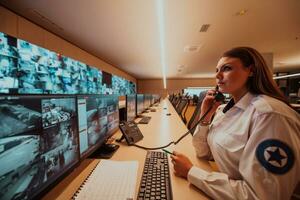 hembra seguridad Guardia operador hablando en el teléfono mientras trabajando a puesto de trabajo con múltiple muestra seguridad guardias trabajando en múltiple monitores foto