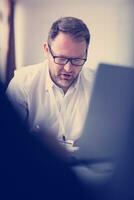 Business man writing notes while working on laptop photo