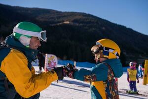 padre preparando a su pequeño hijo por primera vez en una tabla de snowboard foto