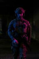 Army soldier in Combat Uniforms with an assault rifle and combat helmet night mission dark background. Blue and purple gel light effect. photo