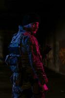 Army soldier in Combat Uniforms with an assault rifle and combat helmet night mission dark background. Blue and purple gel light effect. photo