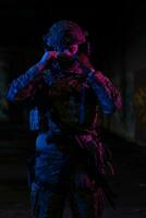 Army soldier in Combat Uniforms with an assault rifle and combat helmet night mission dark background. Blue and purple gel light effect. photo