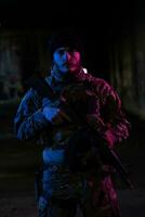 Army soldier in Combat Uniforms with an assault rifle and combat helmet night mission dark background. Blue and purple gel light effect. photo