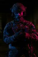 Photo of a fully equipped soldier in black armor tactical vest and gloves standing on black background closeup front view.