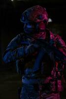 Army soldier in Combat Uniforms with an assault rifle and combat helmet night mission dark background. Blue and purple gel light effect. photo