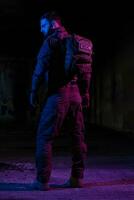 Army soldier in Combat Uniforms with an assault rifle and combat helmet night mission dark background. Blue and purple gel light effect. photo