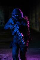 Army soldier in Combat Uniforms with an assault rifle and combat helmet night mission dark background. Blue and purple gel light effect. photo