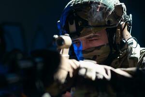 Ejército soldado en combate uniformes con un asalto rifle y combate casco noche misión oscuro antecedentes. azul y púrpura gel ligero efecto. foto