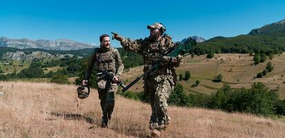 A sniper team squad of soldiers is going undercover. Sniper assistant and team leader walking and aiming in nature with yellow grass and blue sky. Tactical camouflage uniform. photo