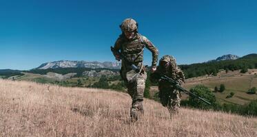 A sniper team squad of soldiers is going undercover. Sniper assistant and team leader walking and aiming in nature with yellow grass and blue sky. Tactical camouflage uniform. photo