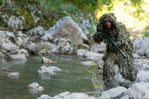 A military man or airsoft player in a camouflage suit sneaking the river and aims from a sniper rifle to the side or to target. photo