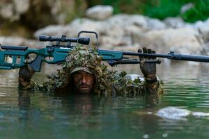 A military man or airsoft player in a camouflage suit sneaking the river and aims from a sniper rifle to the side or to target. photo