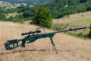 A green military sniper rifle with a scope for long distance tactical modern warfare in yellow grass blue sky photo