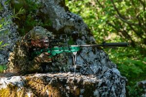 A military man or airsoft player in a camouflage suit sneaking the river and aims from a sniper rifle to the side or to target. photo