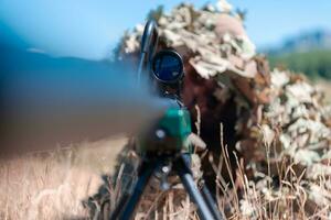 army soldier holding sniper rifle with scope and aiming in forest. war, army, technology and people concept photo