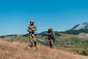 A sniper team squad of soldiers is going undercover. Sniper assistant and team leader walking and aiming in nature with yellow grass and blue sky. Tactical camouflage uniform. photo