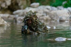 un militar hombre o airsoft jugador en un camuflaje traje furtivo el río y objetivos desde un francotirador rifle a el lado o a objetivo. foto