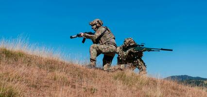 A sniper team squad of soldiers is going undercover. Sniper assistant and team leader walking and aiming in nature with yellow grass and blue sky. Tactical camouflage uniform. photo