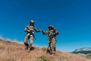 A sniper team squad of soldiers is going undercover. Sniper assistant and team leader walking and aiming in nature with yellow grass and blue sky. Tactical camouflage uniform. photo