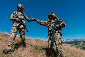 A sniper team squad of soldiers is going undercover. Sniper assistant and team leader walking and aiming in nature with yellow grass and blue sky. Tactical camouflage uniform. photo