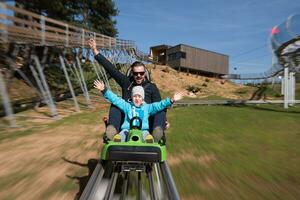 padre e hijo disfrutan conduciendo en montaña rusa alpina foto