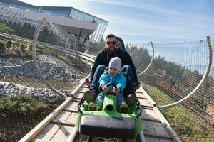 padre e hijo disfrutan conduciendo en montaña rusa alpina foto