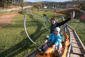 madre e hijo disfrutan conduciendo en una montaña rusa alpina foto