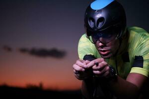 atleta de triatlón montando bicicleta rápido por la noche foto