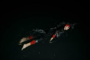 atleta de triatlón nadando en la noche oscura con traje de neopreno foto