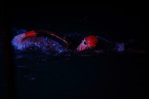 atleta de triatlón real nadando en la noche oscura foto