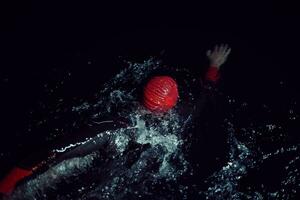 atleta de triatlón nadando en la noche oscura con traje de neopreno foto