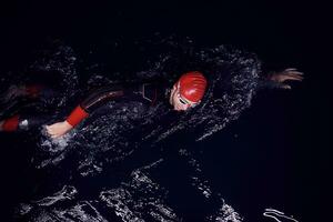 triathlon athlete swimming in dark night  wearing wetsuit photo