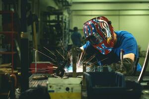 soldador profesional de la industria pesada que trabaja dentro de la fábrica, usa casco y comienza a soldar. enfoque selectivo foto