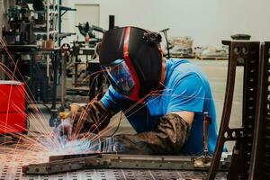 soldador profesional de la industria pesada que trabaja dentro de la fábrica, usa casco y comienza a soldar. enfoque selectivo foto