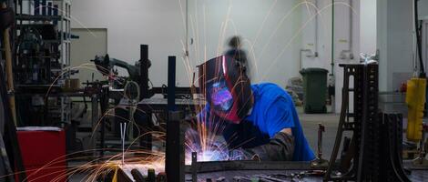 soldador profesional de la industria pesada que trabaja dentro de la fábrica, usa casco y comienza a soldar. enfoque selectivo foto