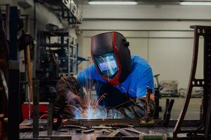 Professional Heavy Industry Welder Working Inside factory, Wears Helmet and Starts Welding. Selective Focus photo